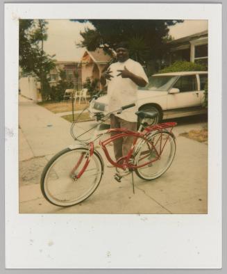 [Man posing beside red and white bicycle making hand gestures]
