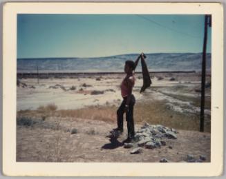 Grant, N.M. [Man posing in rocky landscape holding shirt above his head]
