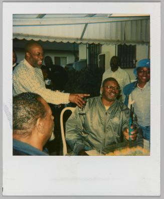 [Man lighting barbeque lighter, man laughing and pointing with wine glass in hand]
