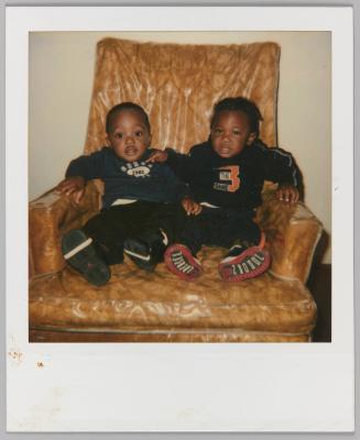[Two toddler boys sitting on yellow chair covered by plastic]
