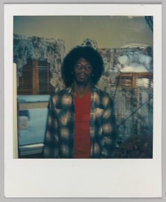 [Man posing indoors in front of floral curtains in red shirt and unbuttoned flannel shirt]

