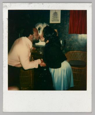 [Man in yellow shirt and woman in blue dress kissing on the lips and holding hands]

