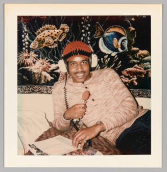 [Man smiling with headphones and pink microphone]