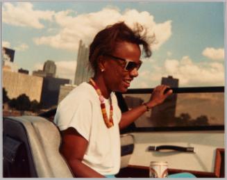 Renee Aug 1987 Rickey's Boat On the river Pgh. Pa. [Profile of woman in sunglasses with bead necklace and white t-shirt sitting in a boat on a sunny day]