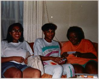 Erica Renee Cheryl [Three women sitting on a couch and smiling, woman on right in orange shirt]