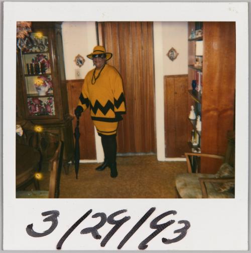 3/29/93 [Woman standing inside wearing a yellow and black dress, she is holding an umbrella]