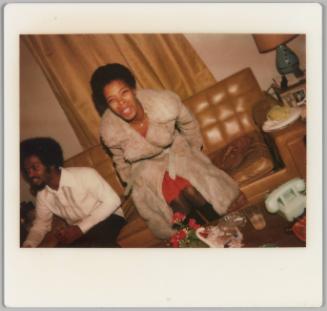 [Woman in fur coat getting up from brown leather couch where a man is seated, blue telephone on table]