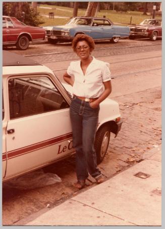 [Woman posing in front of car wearing aviator glasses and blue jeans]

