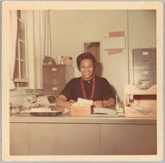 [Woman sitting and smiling at desk sifting through cards in box]
