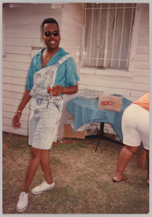 [Man posing wearing short-overalls, holding a wine glass]
