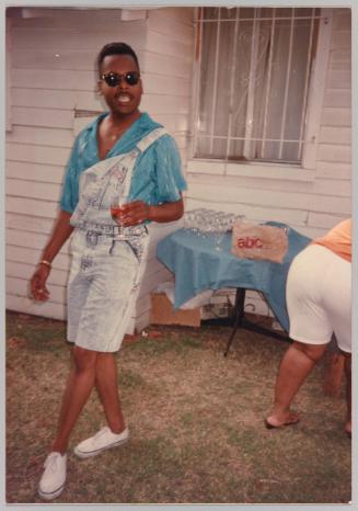 [Man posing wearing short-overalls, holding a wine glass]
