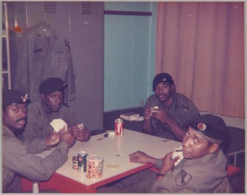 [Men in uniform sitting around table playing cards and drinking cola]
