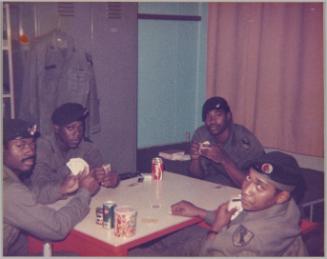 [Men in uniform sitting around table playing cards and drinking cola]
