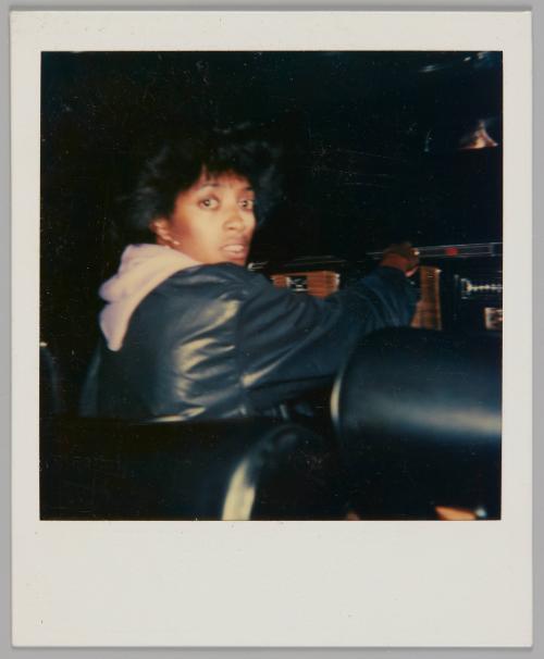 [Woman in black jacket with light-coloured hood popping out from underneath, she is turning back to look at the camera]