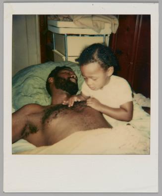 [Shirtless man asleep beside a child who is looking at and touching his chest hair]