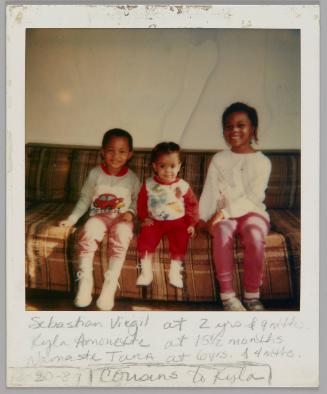 Sebastian Virgil at 2 yrs & 9 mths. Kyla Amonette at 15 1/2 months Namaste Tara at 6 yrs & 4 mths. [12-30?]-87 Cousins to Kisla [Three children sitting on brown plaid couch]