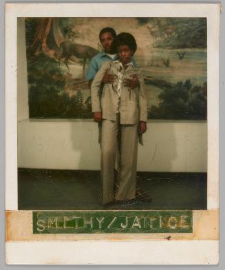 Smithy/Janice Nov. 2[9?] 75 [Man  in blue collared shirt holding person in grey suit from behind, there is a picture of a forest with deers behind them]