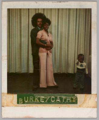 Burke/Cathy [Man holding woman in pink outfit from behind with a young child to the right, curtain behind them]