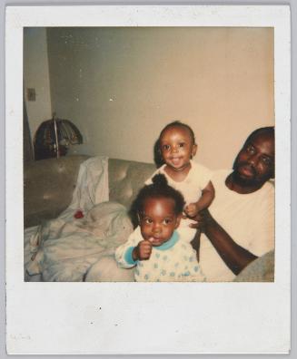 [Man holding on baby behind toddler girl in blue floral turtleneck]