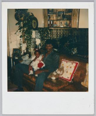 [Man sitting on couch with toddler girl sitting in his lap, stuffed animal beside him]