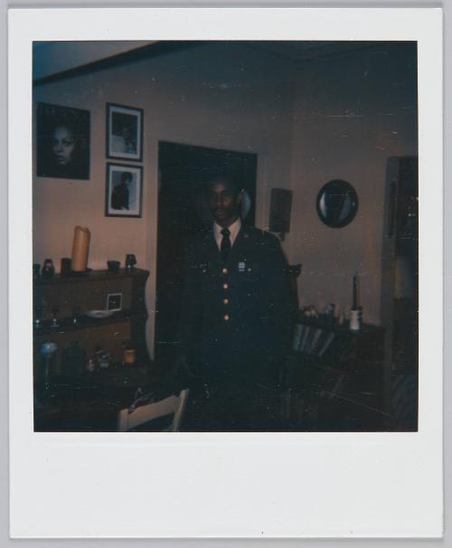 [Underexposed image of young man standing in living room area wearing a cardigan]
