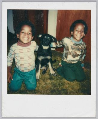 [Twin boys smiling, black dog sitting in between them]