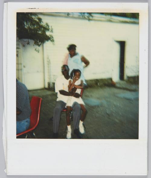 [Man wearing sunglasses sitting on red chair with little girl sitting on his lap]