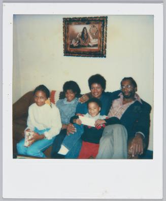 [Family of five gathered on couch, little boy in front holds an envelope]