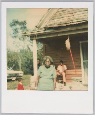 [Elderly woman in blue striped tshirt slightly hunched over, house in the background]