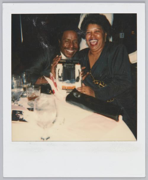 [Man and women in black sitting at table, man holds up packaged Walkman]