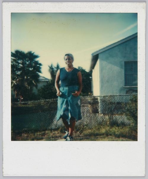 [Woman posing near fence in denim skirt and navy blue tank top]