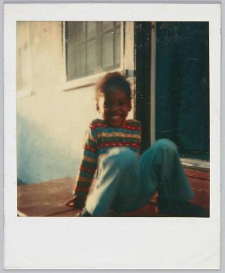 [Little girl in striped sweater sitting on doorstep with big grin]