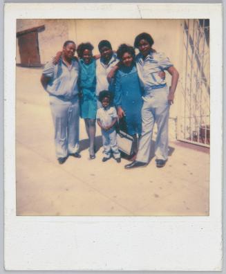 [Family gathered with arms around each other on sidewalk]