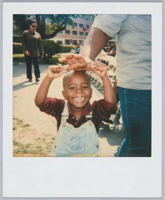 [Toddler boy with huge grin on his face holding adult's hand above his head]