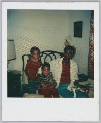 [Two little boys sitting next to young man on bed]