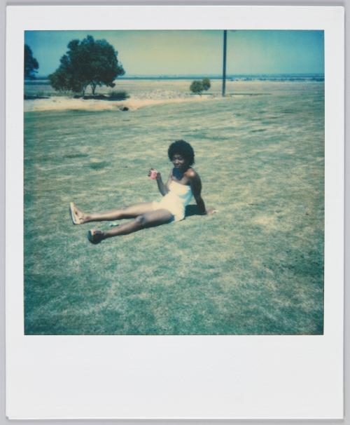 [Woman in white shorts and top lounging on grass with a drink in hand]