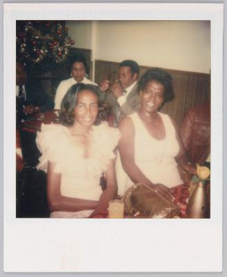 [Two women in white sitting at table with Christmas tree in the background]