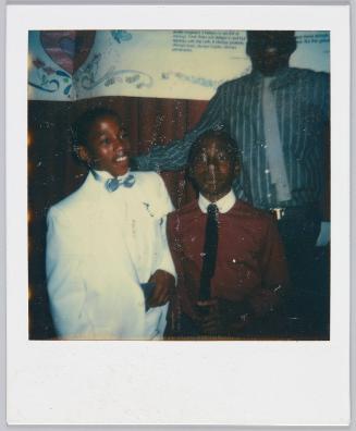 [Three boys in formal attire, boy on right wearing all white suit and light blue bowtie]