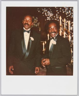 [Two men in black tuxedos and pink boutineers, both have moustaches]