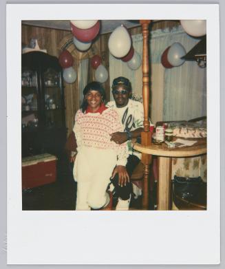 [Woman in red and white patterened sweater standing in between man's legs smilling]