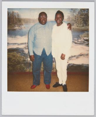 [Man wearing glasses and button up shirt with arm around woman in white pants and top]