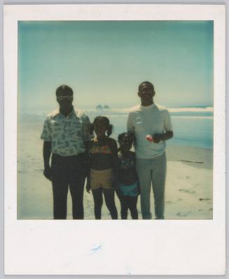[Group of four standing on beach, two kids in the middle wearing their swimsuits]