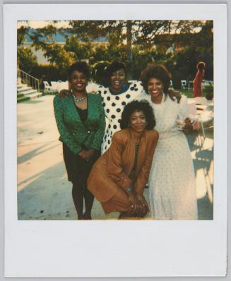 [Group of four women posing outside, woman in middle wears a black and white polkadot dress]