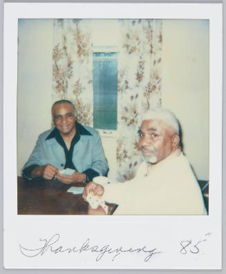 Thanksgiving 85 [Two older men sitting at table playing a game of cards]
