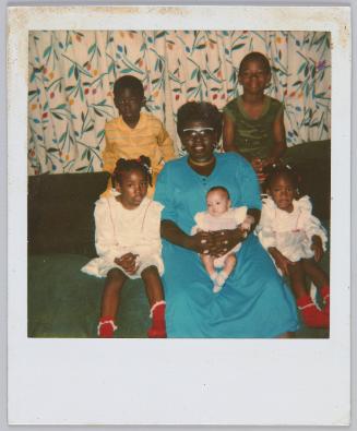 [Woman in green dress surrounded by four kids on couch, woman holding infant in lap]