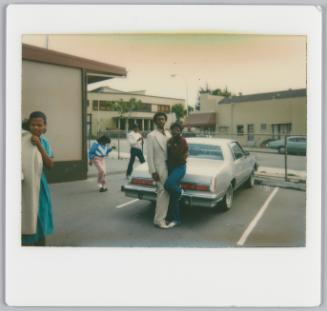 [Couple arm-in-arm posing in parking lot, in front of white car]