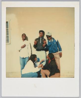 [Three young men holding up hands signs posing behind two young women squatting]