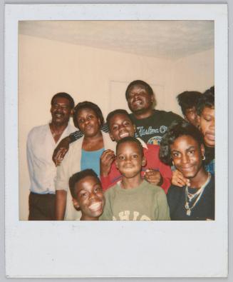 [Two men, two women and three children together in a group smiling in white room]