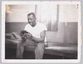 Bon temps -62- to [illeg.] with love [illeg.] [Man sitting on couch wearing a white t-shirt with cigarette hanging from his mouth looking inside a handheld container]