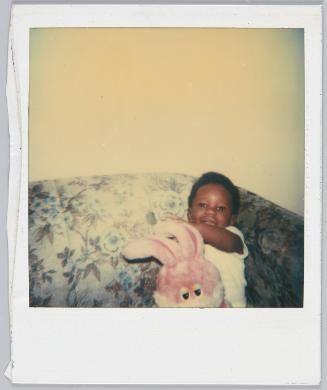 [Child sitting on floral couch holding a pink toy bunny]